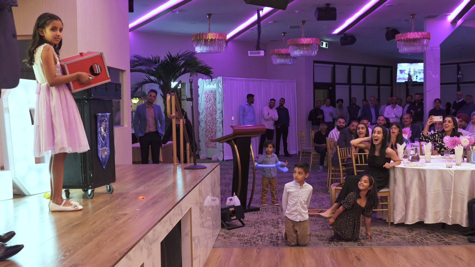 Children kneeling at the front of a community hall stage during a birthday magic show