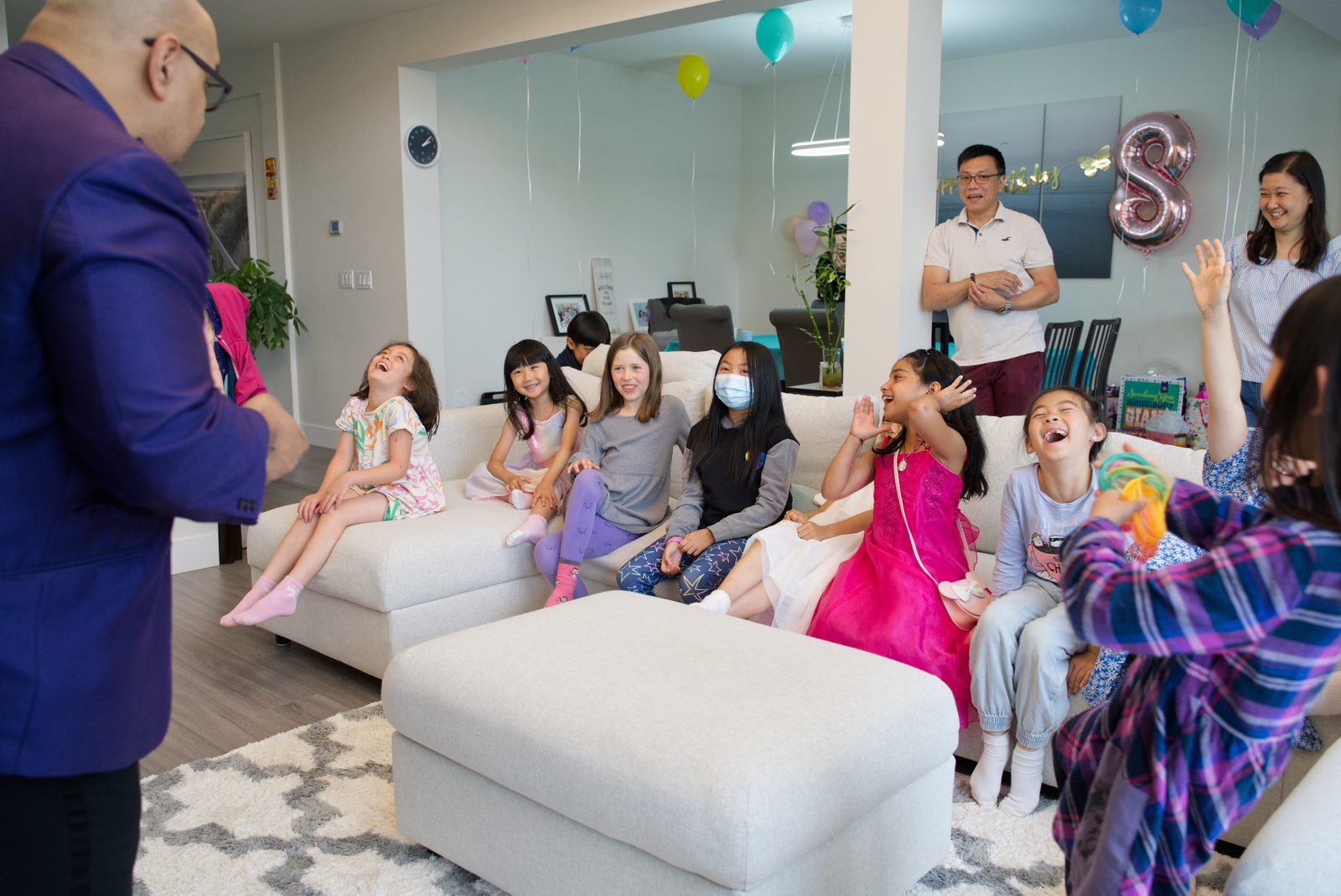 Kids on a living room couch reacting to a close-up magic trick at a house birthday party