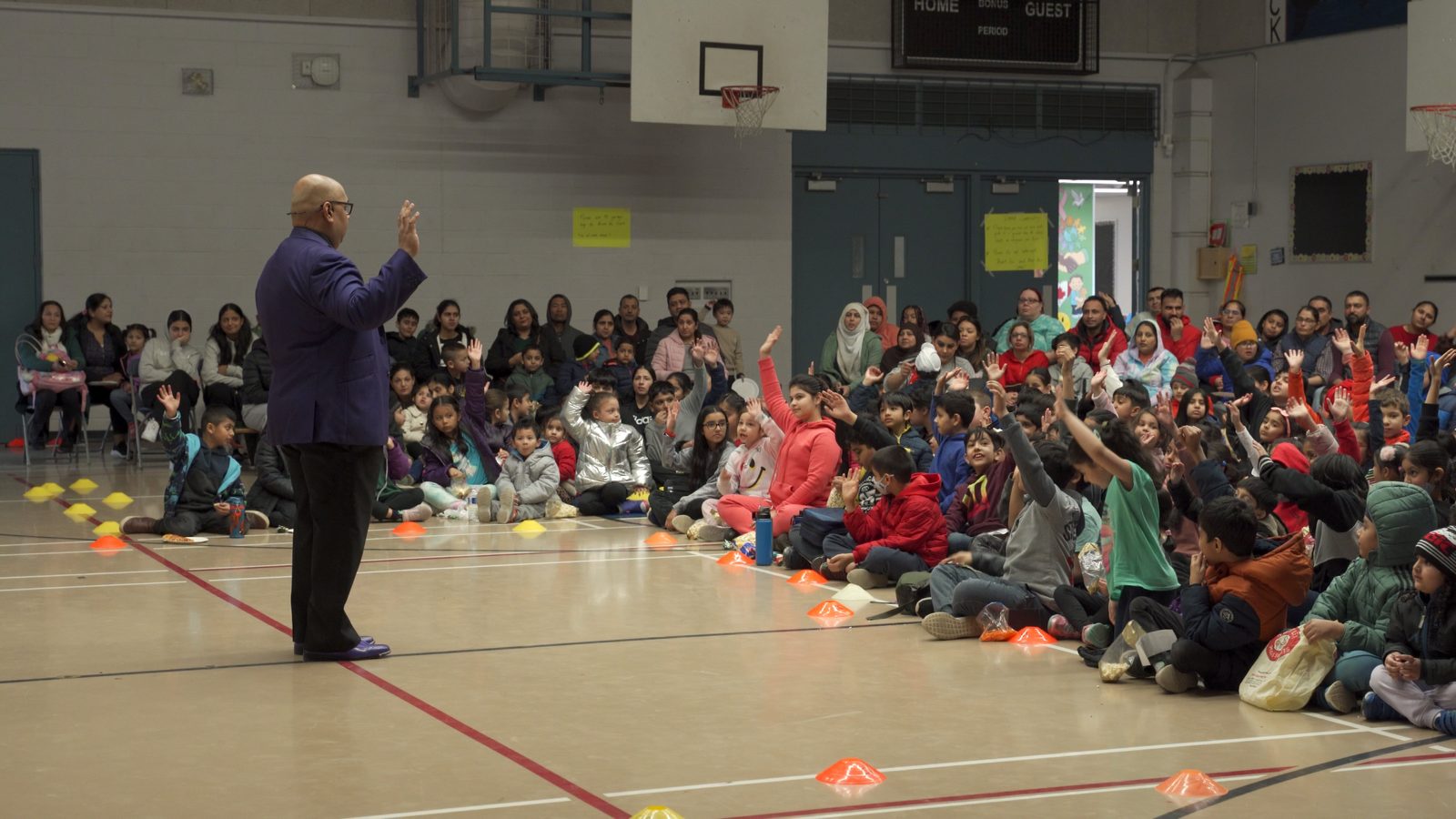 A school gym full of students and parents laughing at a magic assembly